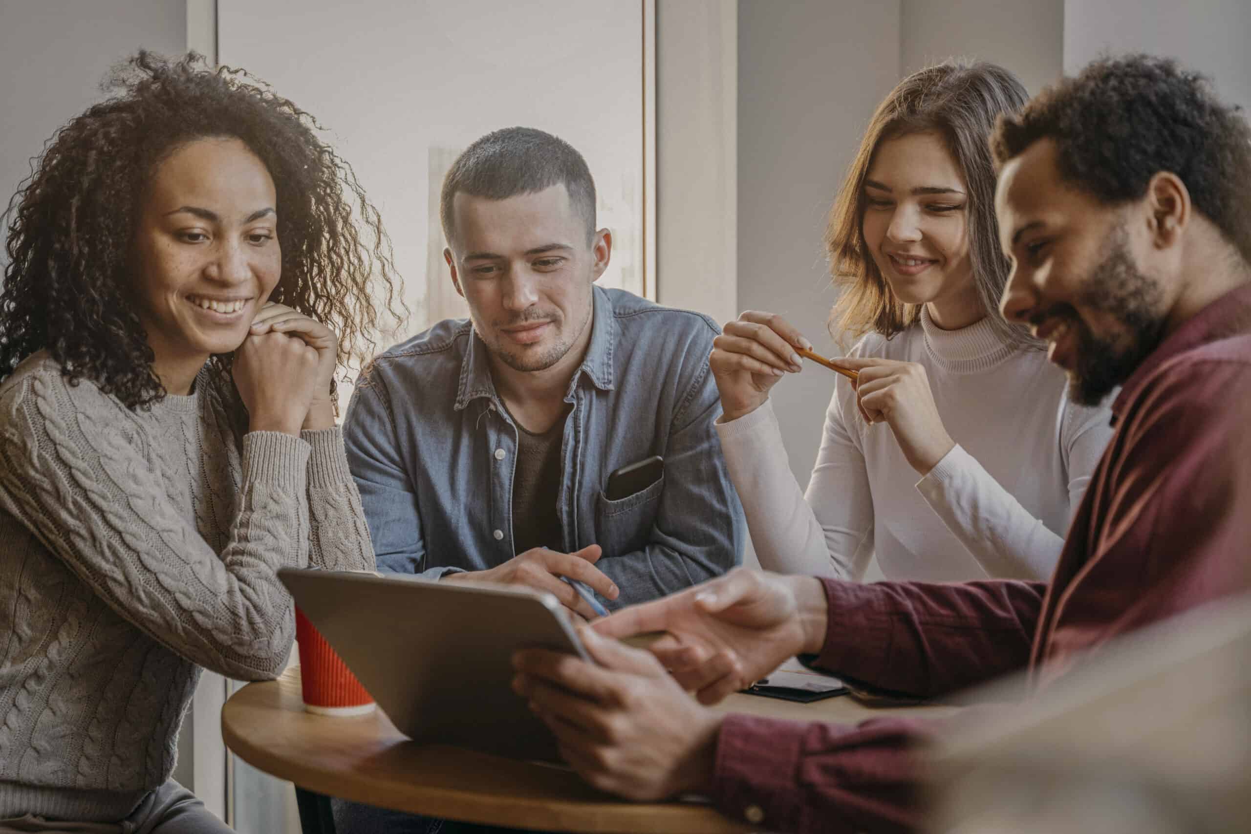 Group of people sitting together around a table collaborating and looking at a tablet, representing partnership and teamwork
