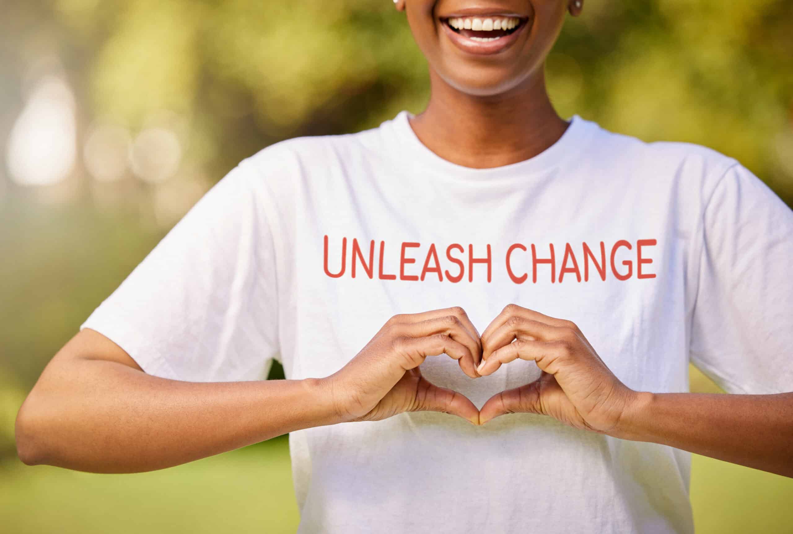 Person wearing a shirt that says “Unleash Change” making a heart shape with their hands, symbolizing compassion and volunteering